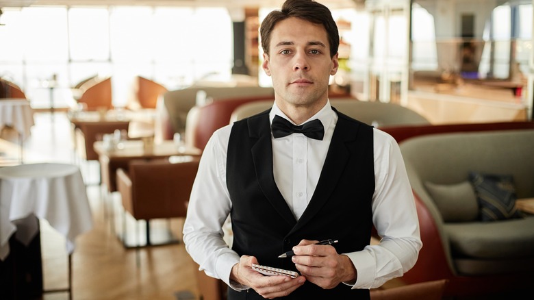 Male waiter wearing formal uniform holding a notepad ready to take an order