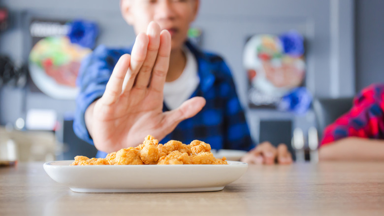 Boy holding up hand to reject a plate of food