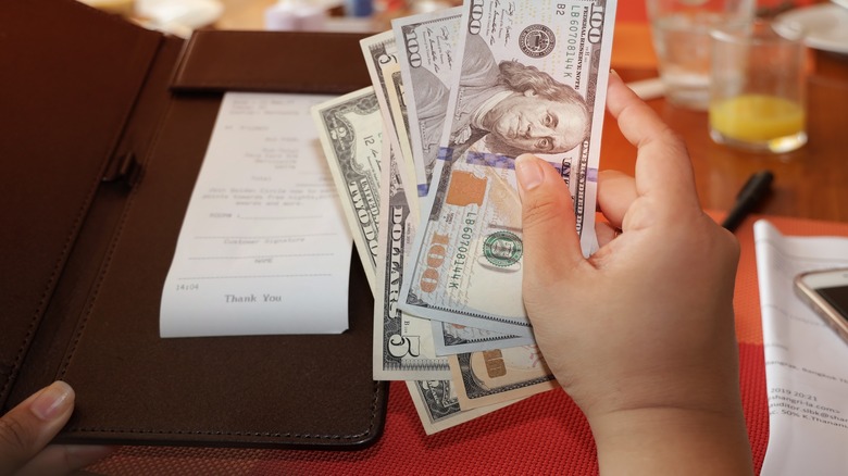 A pair of hands holding a restaurant check and several dollar bills