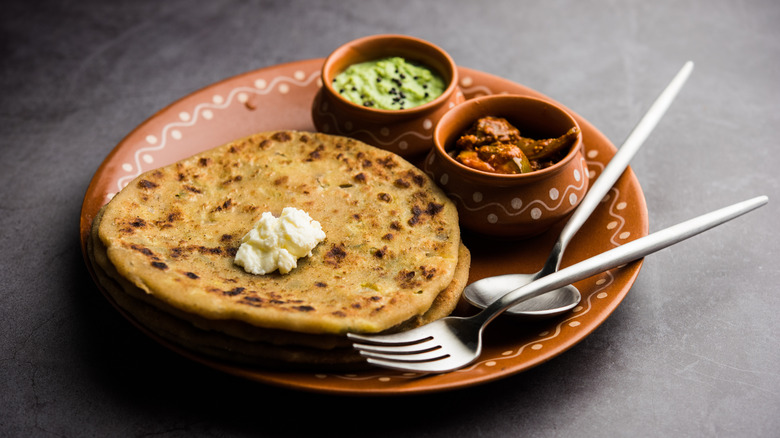 Indian flatbread with accoutrements placed in coordinated bowls and served on a decorative plate with utensils