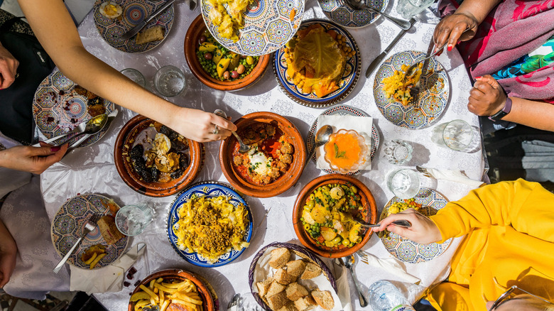 Top view of several diners reaching for food from a Moroccan spread assembled on a large round table