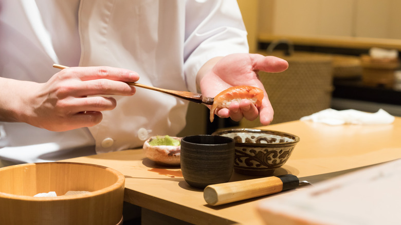 A Japanese chef preparing sushi at a restaurant and smothering a piece with soy sauce