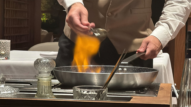 A server preparing a dish with fire at a tableside presentation
