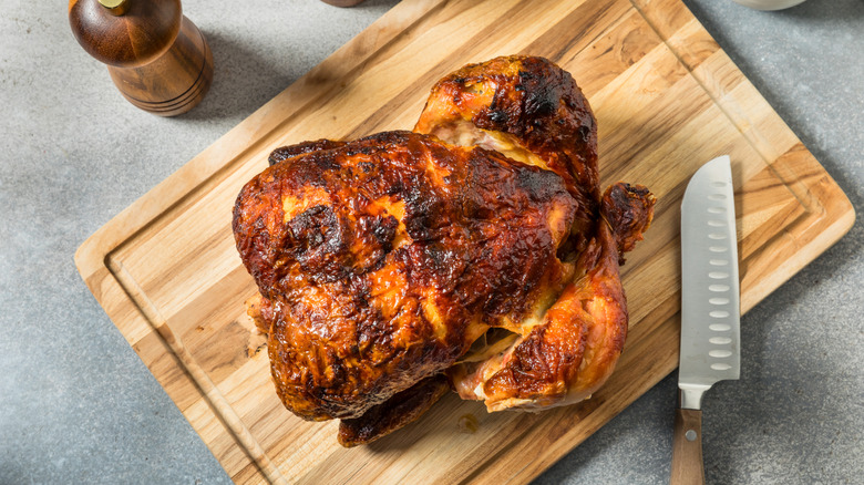 Rotisserie chicken with dark skin on wooden cutting board