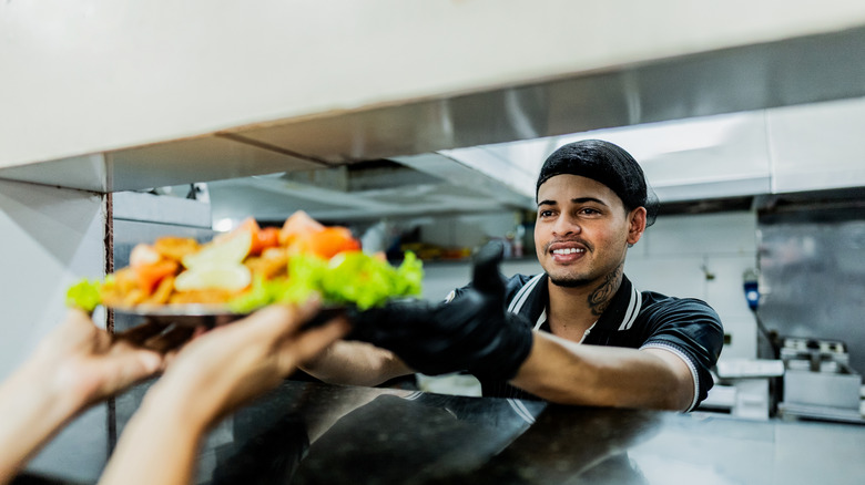 chef passing platter with food to waiter at restaurant
