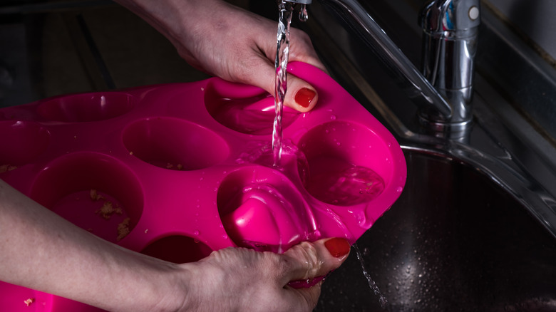 A pair of hands washing a silicone cupcake mold under a running tap