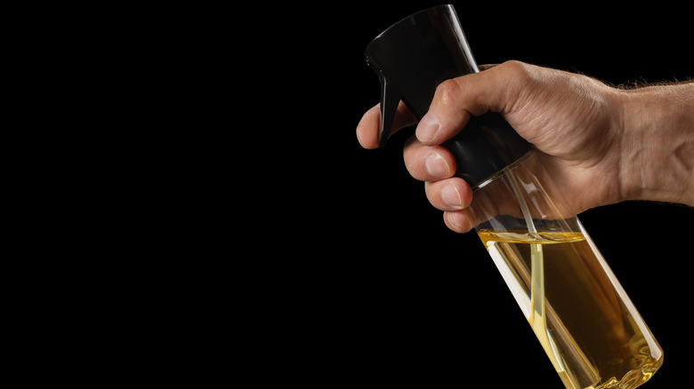 Hand holding a cooking spray against a black background