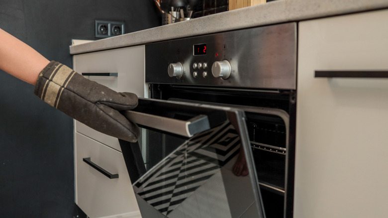 Hand wearing an oven mitt opening the oven in a modern kitchen