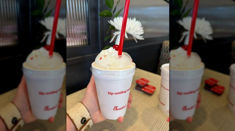 Hand holding Chick-fil-A peach milkshake in cup with straw