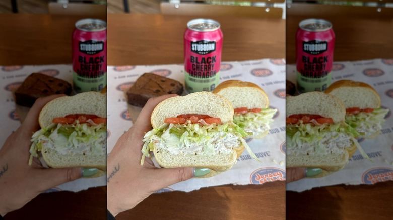 Hand holding Jersey Mike's Chicken Salad Sub, with can of drink and brownie in background