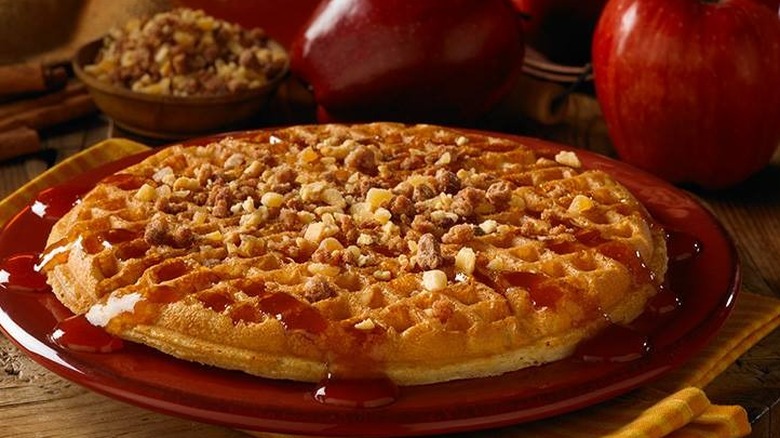 Waffle on a red plate with apples in the background