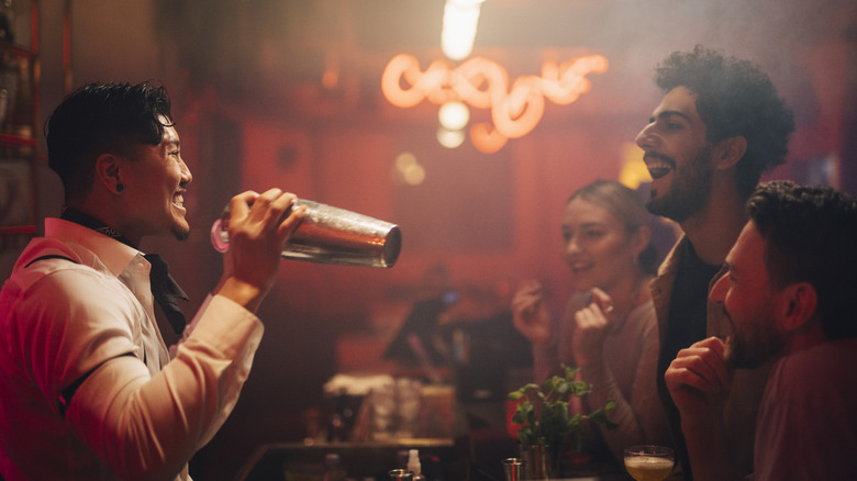 A bartender shaking cocktails with customers watching