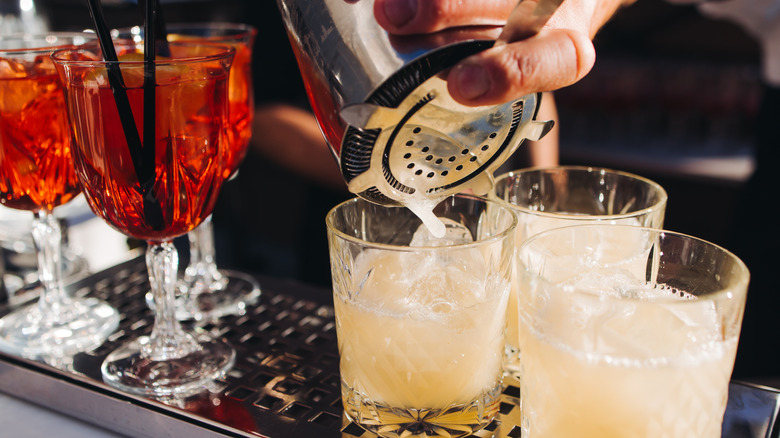 Bartender pouring some shaken cocktails into tumblers
