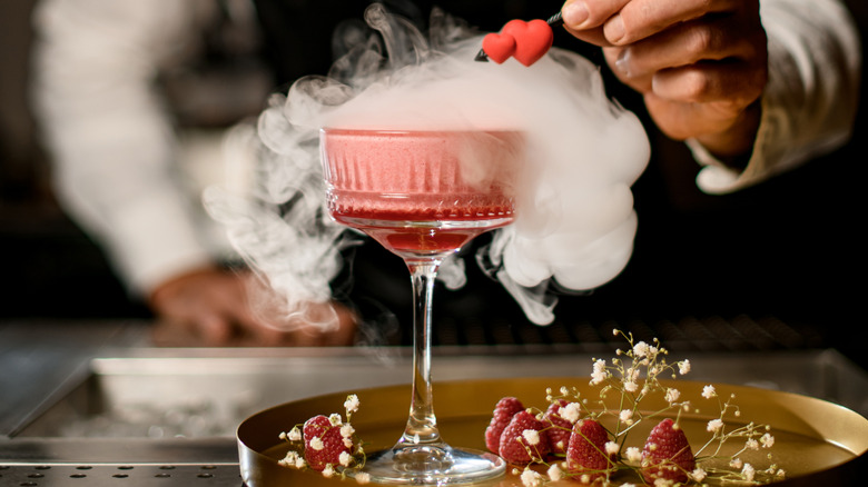 Pink cocktail presented with dry ice and strawberry decor