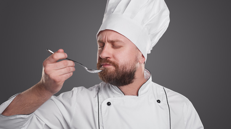 A male chef with white hat smelling a silver spoon