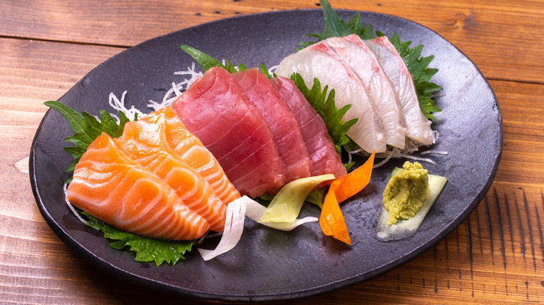 Dark oval plate of sashimi with garnish.