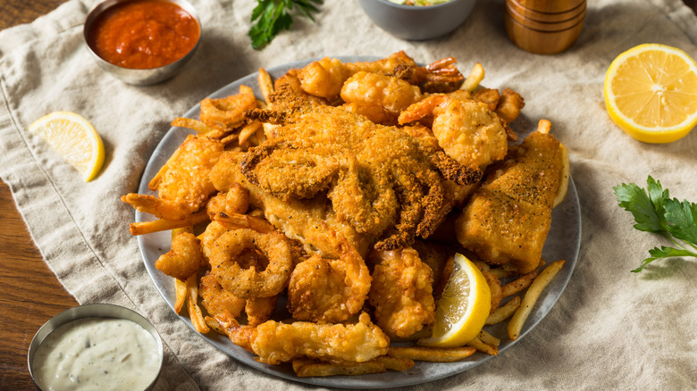 Platter of fried seafood on cloth with sauce and lemon.