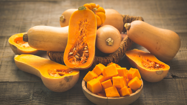 Various whole, halved, and chopped butternut squash displayed on wood
