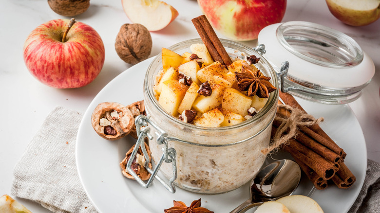 Fall-inspired overnight oats in a glass jar with spices and apples all around