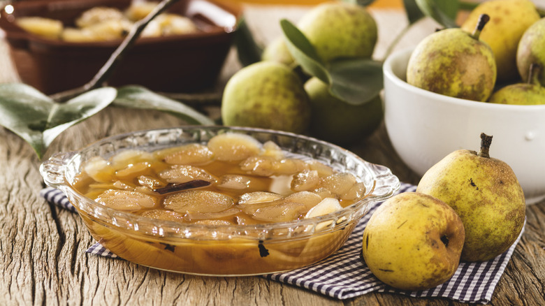 Pear compote cooling in a glass pie dish surrounded by pears