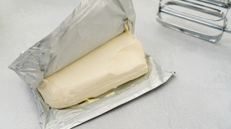 Opened brick of cream cheese next to metal beaters
