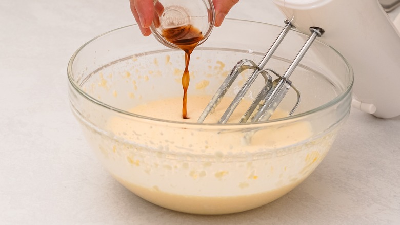 Pouring vanilla extract from small bowl into large mixing bowl of batter