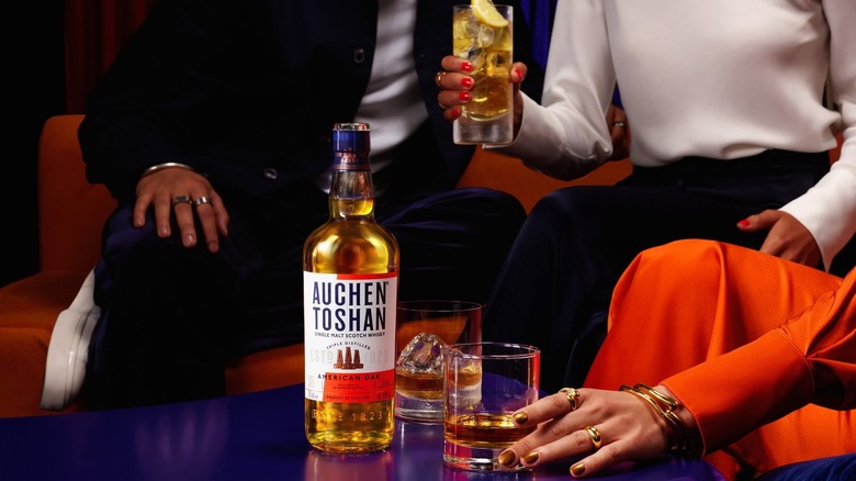 A bottle of Auchentoshan American Oak on a colorful table surrounded by drinkers