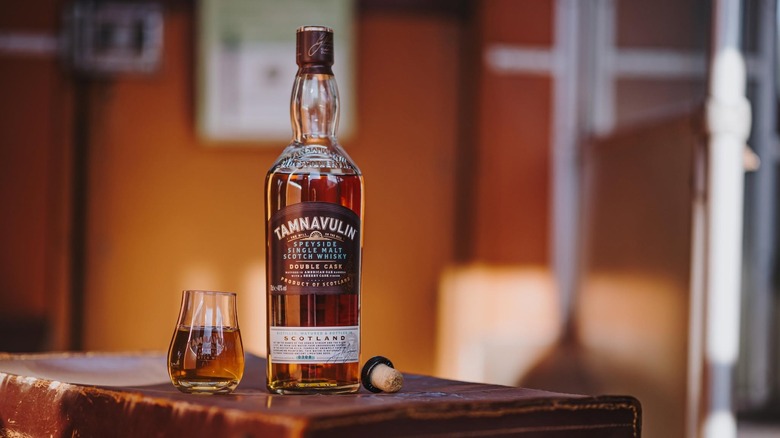 A bottle of Tamnavulin Double Cask placed on a rustic surface next to a filled branded glass