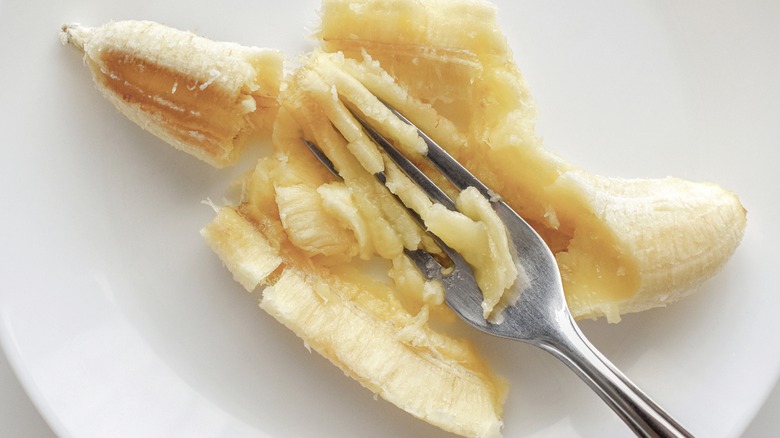 Smashing banana on plate with fork