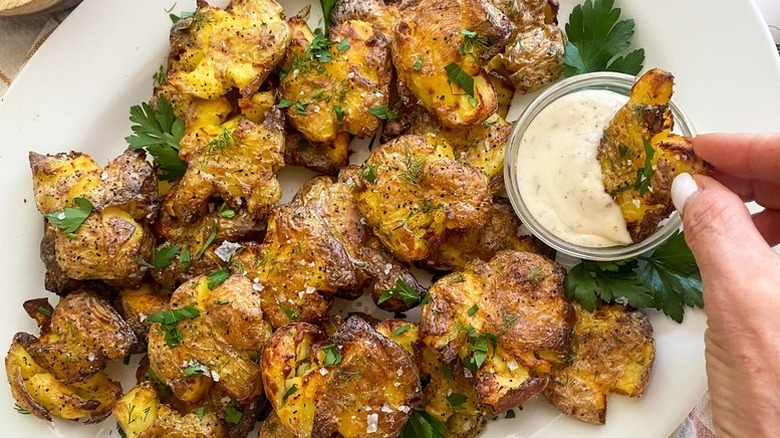 Smashed potatoes on plate with creamy dip and parsley garnish