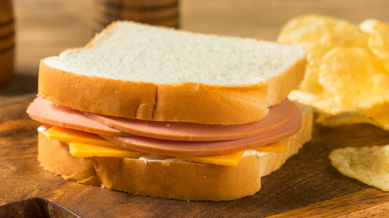 Homemade Bologna and Cheese Sandwich with Chips on a wooden board
