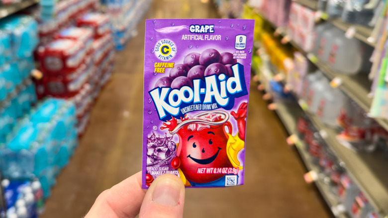 hand holding Pack of Grape flavored Kool Aid drink mix in store