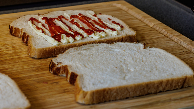 Bread slices on wooden board, one of which has ketchup and mayonnaise
