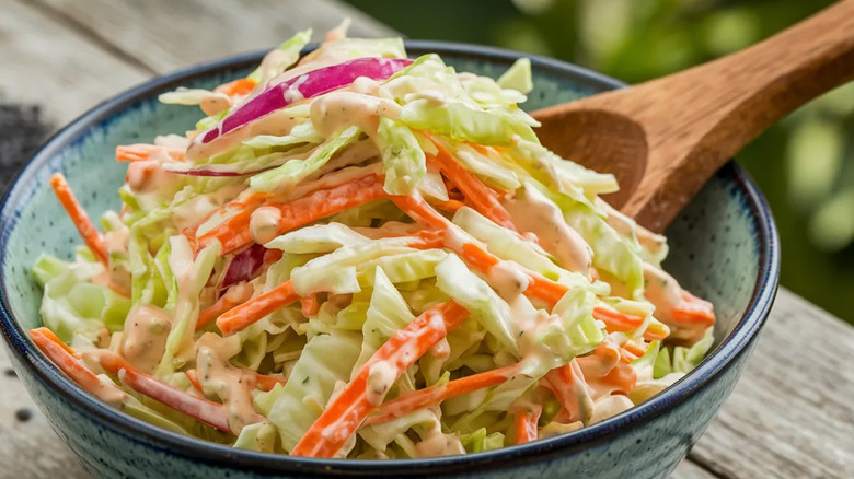 A bowl of colorful coleslaw with a wooden spoon