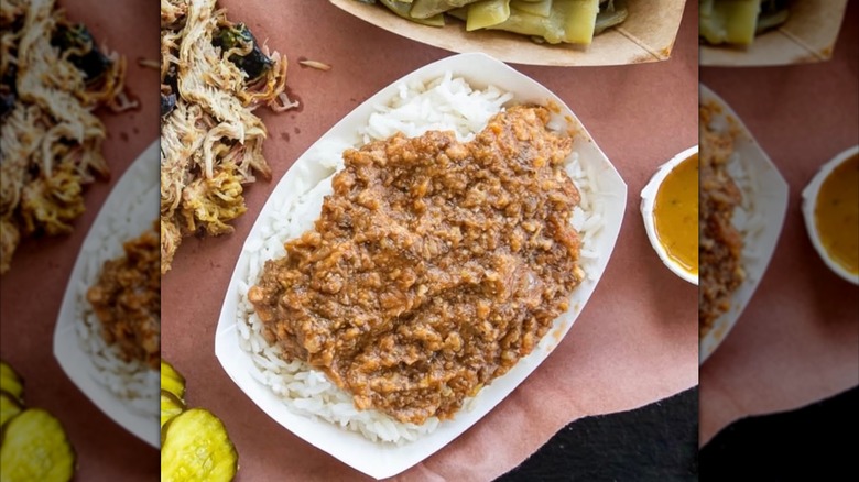 A container of rice and hash with mustard barbecue sauce on the side