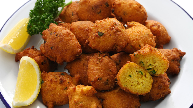 A bowl of hushpuppies garnished with lemon wedges and parsley