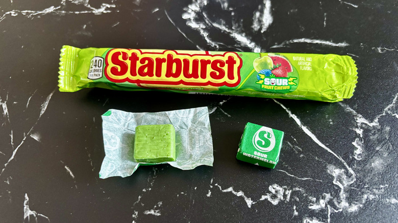 Starburst candy package next to wrapped and unwrapped sour watermelon Starburst