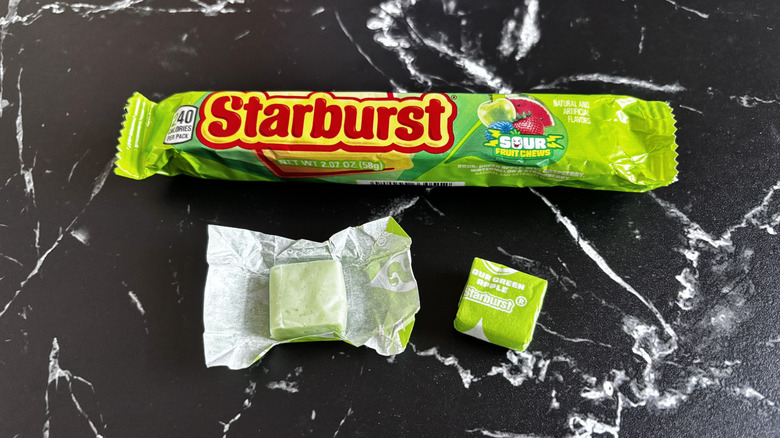 Starburst candy package next to wrapped and unwrapped sour green apple Starburst