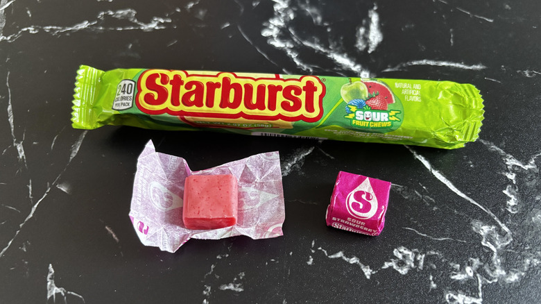 Starburst candy package next to wrapped and unwrapped sour strawberry Starburst