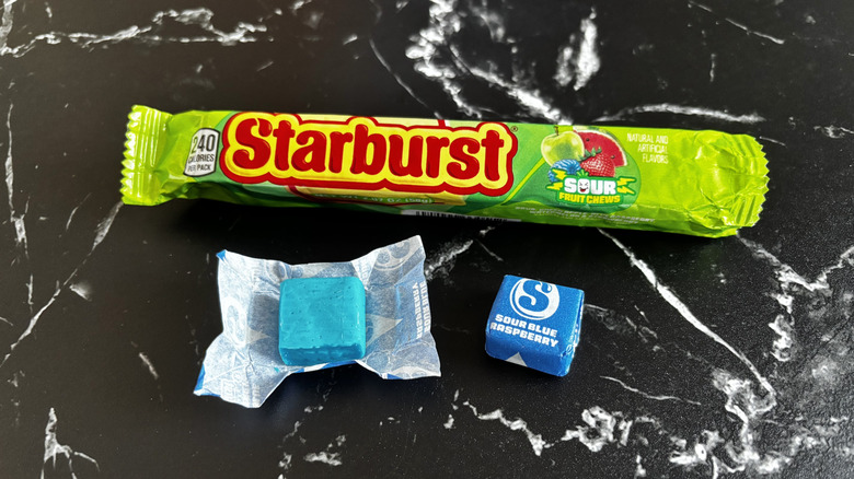 Starburst candy package next to wrapped and unwrapped sour blue raspberry Starburst