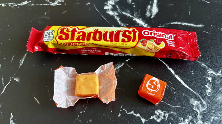 Starburst candy package next to unwrapped and wrapped orange Starburst