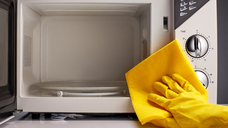 Woman's hand wearing yellow rubber gloves and cleaning the microwave