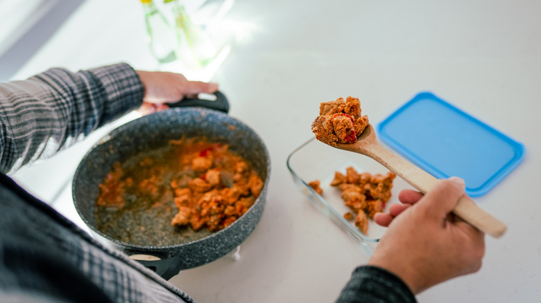 A pair of hands packing food in a glass container with a blue lid