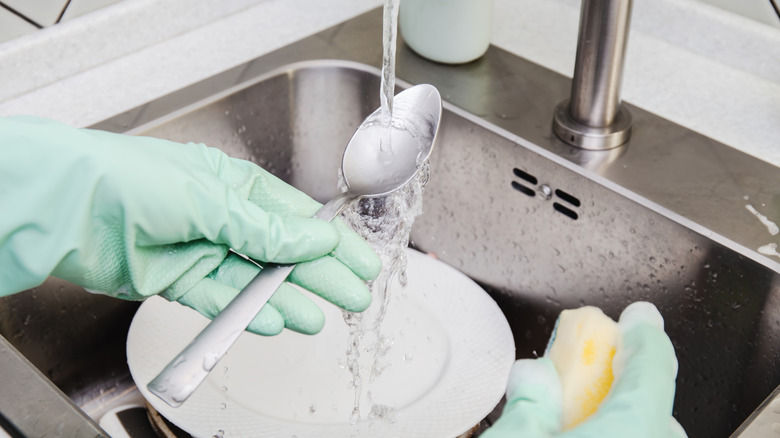 Hand washing a spoon under running water in the sink