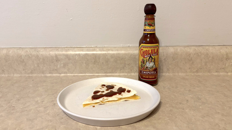 Cholula chipotle hot sauce on quesadilla on white plate on countertop