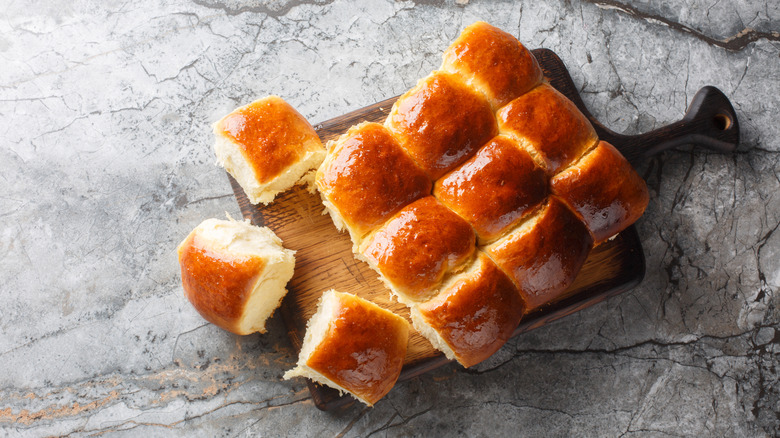 Bread rolls placed on a wooden platter against a gray background
