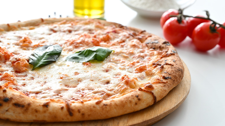 Ready-to-cook pizza placed next to cherry tomatoes and oil on a white table