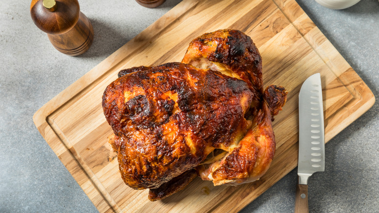 Rotisserie chicken placed next to a knife on a wooden cutting board