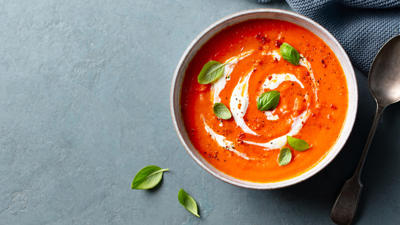 Creamy tomato soup garnished with fresh leaves and placed on a gray background