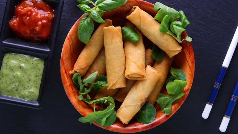 Spring rolls garnished with fresh leaves and placed next to an array of sauces